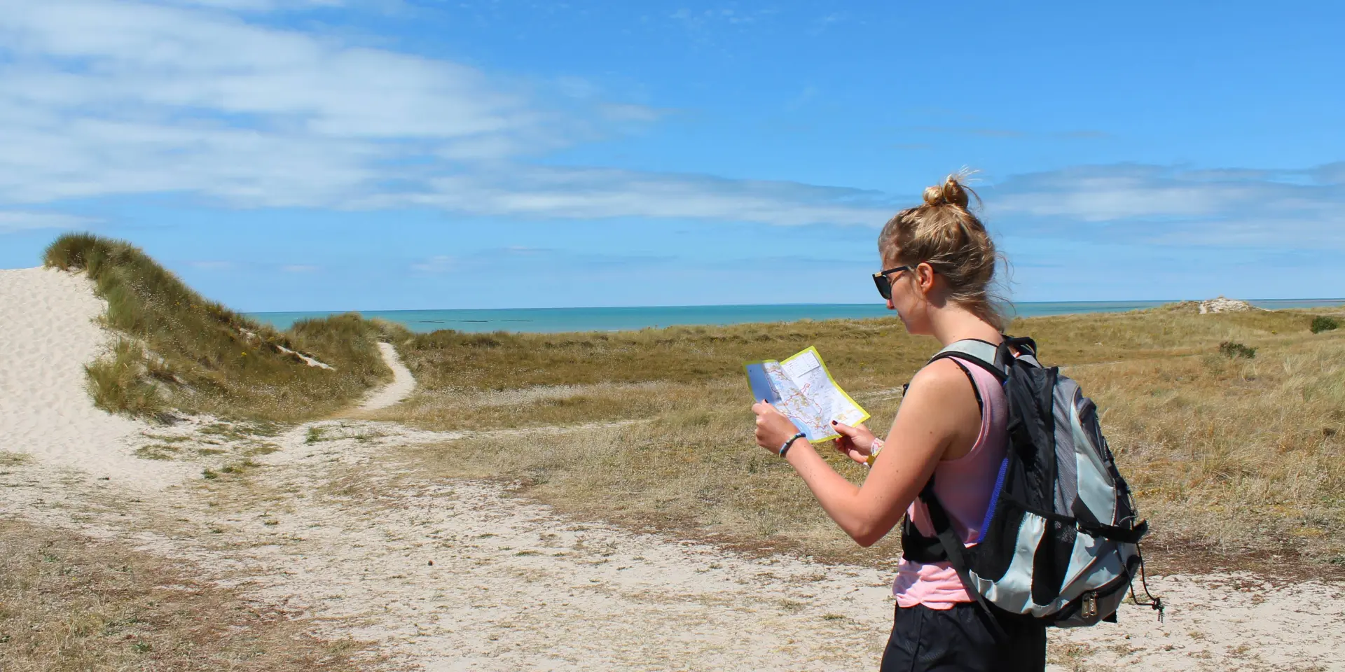 Woman sitting on a rock by the sea, holding a book and a mobile phone