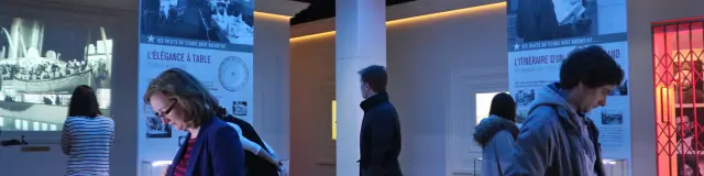 Menschen untersuchen Objekte in einem Museum mit Postern und blauen Deckenlichtern