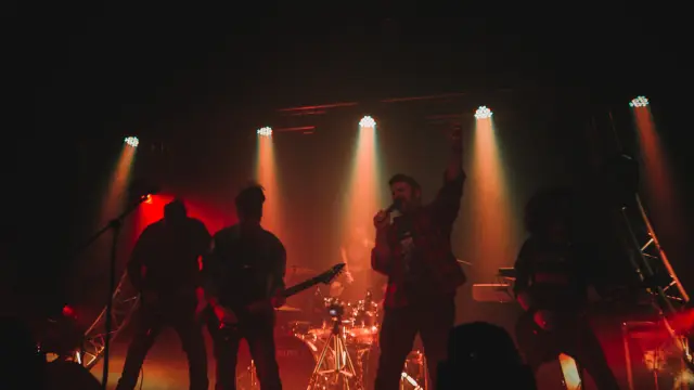 Groupe de musique jouant sur scène avec des projecteurs rouges