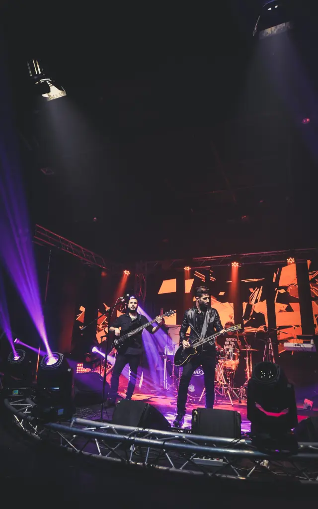 Groupe de rock jouant sur scène avec des guitares électriques sous des lumières colorées