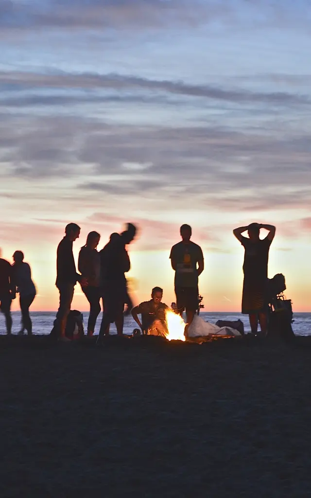 Un groupe de personnes autour d'un feu de camp sur une plage au coucher du soleil