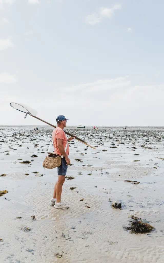 Ein Mann mit einem Schmetterlingsnetz an einem schlammigen Strand