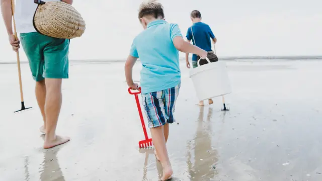 Enfants marchent sur la plage avec des seaux et des pelles pour la pêche à pied à Agon Coutainville