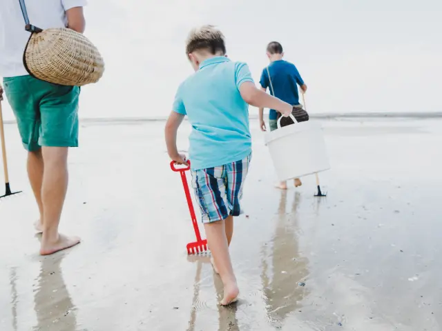 Enfants marchent sur la plage avec des seaux et des pelles pour la pêche à pied à Agon Coutainville