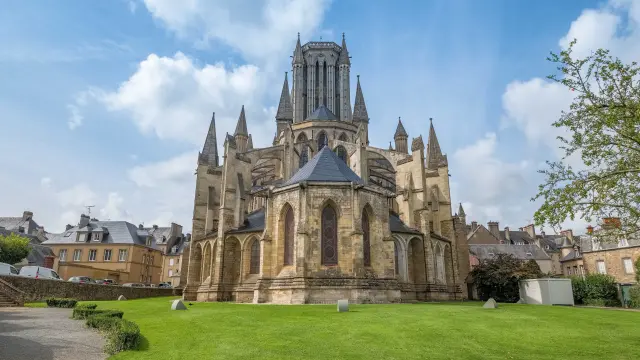 Cathédrale gothique avec des tours pointues et des vitraux, entourée de bâtiments anciens et d'un parc