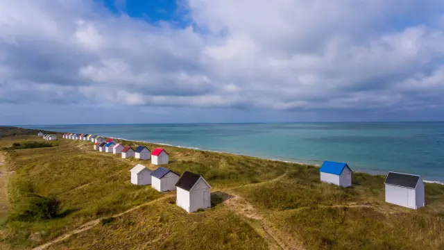 Eine Reihe bunter Strandhütten auf einem grasbewachsenen Hügel in der Nähe des Meeres