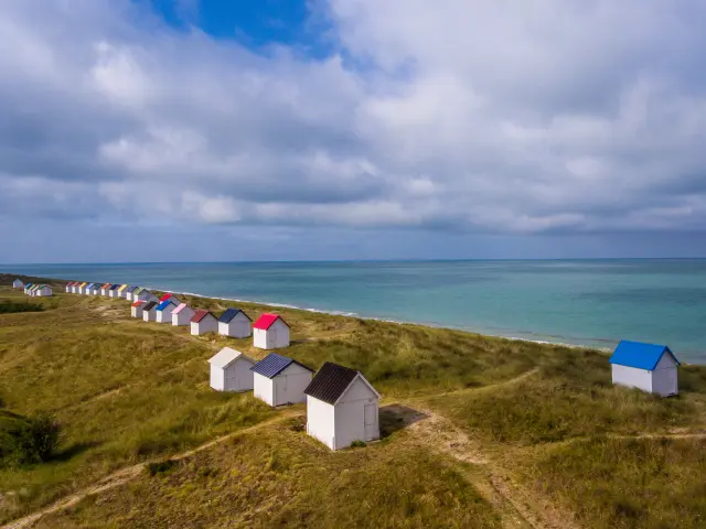 A row of colorful beach huts on a grassy hill near the sea