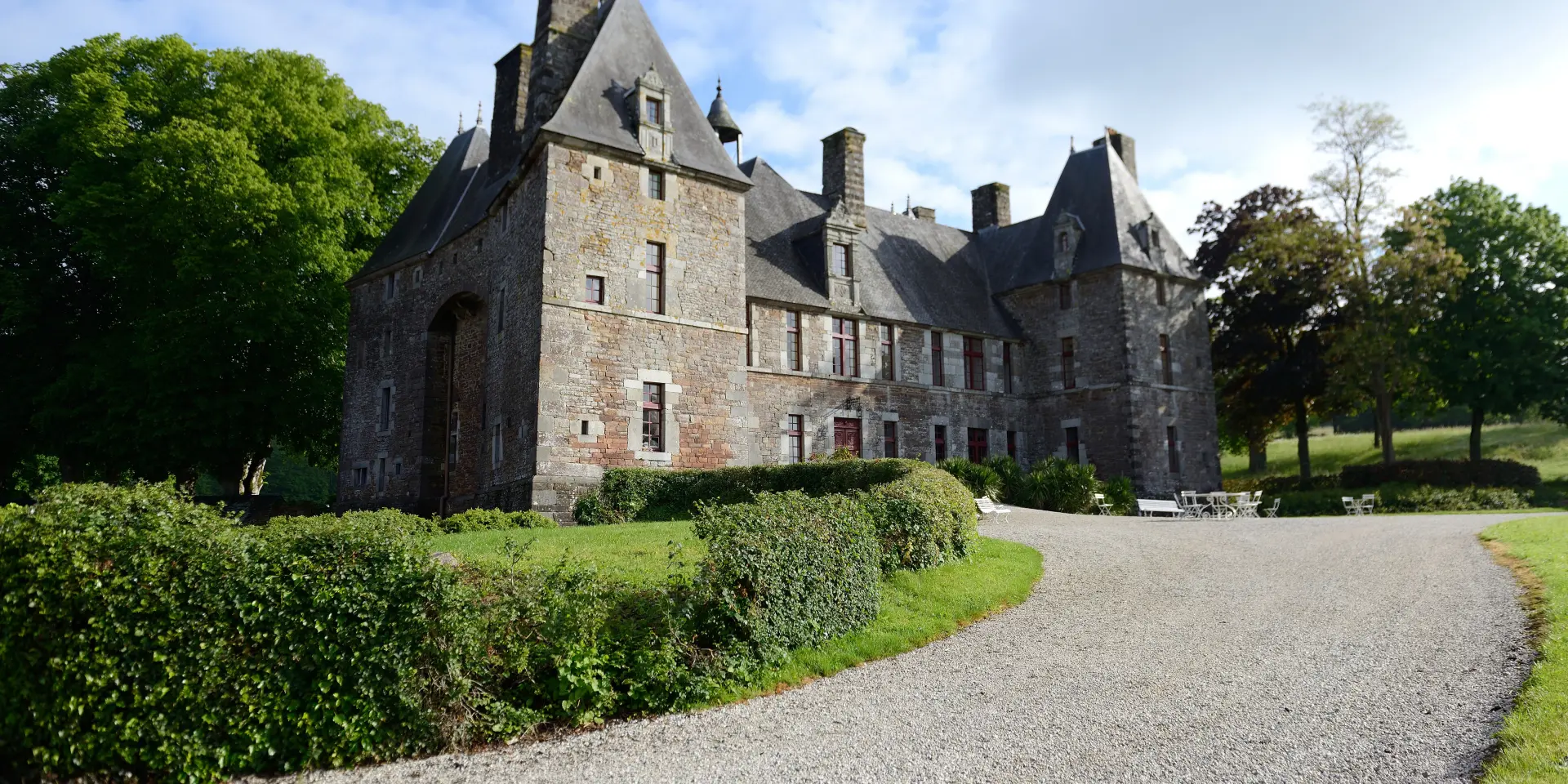 Château de Cerisy La Salle avec des toits pointus et des cheminées, entouré de buissons et d'arbres