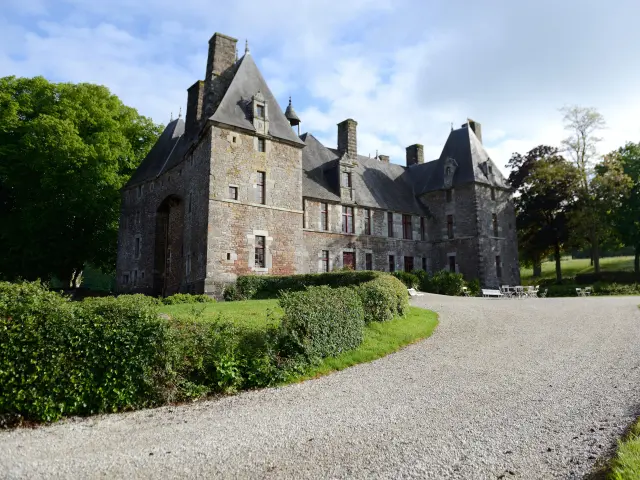 Stone castle with pointed roofs and chimneys, surrounded by bushes and trees
