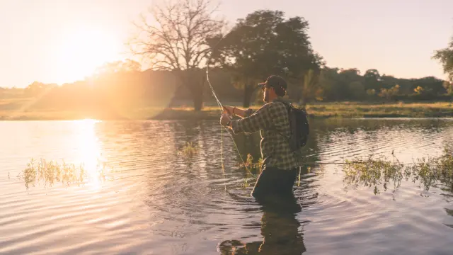 Un pêcheur debout dans l'eau avec une canne à pêche au coucher du soleil