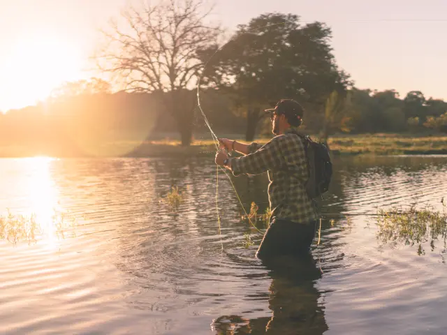 Un pêcheur debout dans l'eau avec une canne à pêche au coucher du soleil