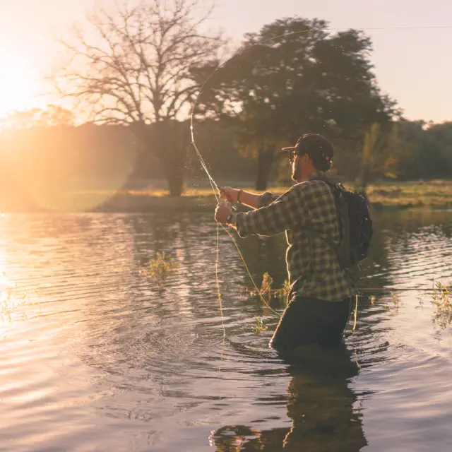Un pêcheur debout dans l'eau avec une canne à pêche au coucher du soleil