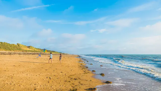 Plage de sable avec des voiliers amarrés près du rivage et des personnes se promenant