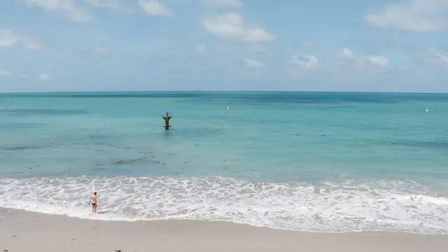 Deux voiliers amarrés près d’une plage avec des reflets orangés sur l’eau au coucher du soleil