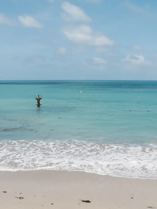 Deux voiliers amarrés près d’une plage avec des reflets orangés sur l’eau au coucher du soleil