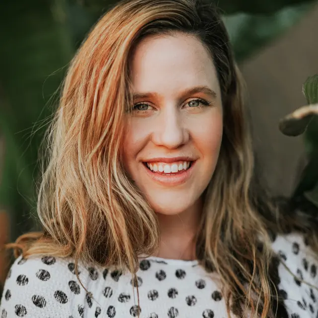 Femme souriante avec des cheveux blonds et bruns, portant un haut à pois