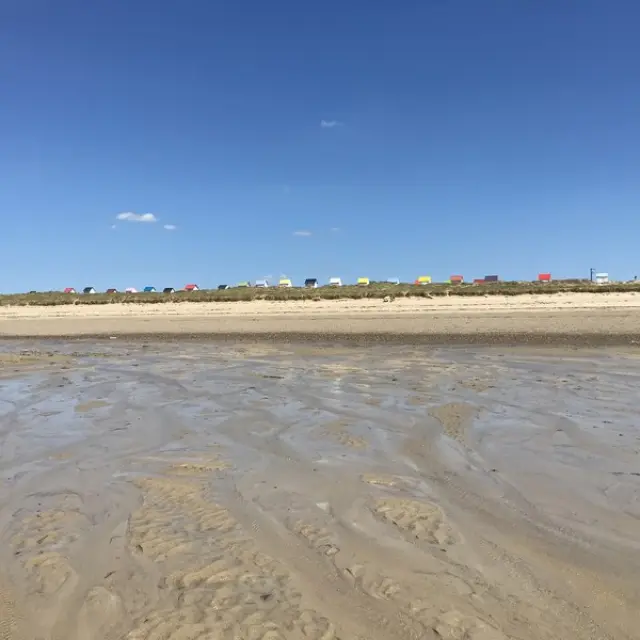 Plage de sable avec traces de pas et voiliers amarrés à l’horizon au coucher du soleil