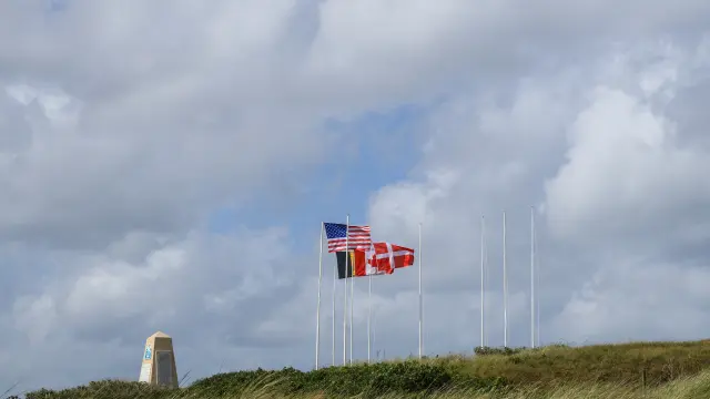 Phare blanc avec drapeau américain sur une colline herbeuse sous un ciel nuageux