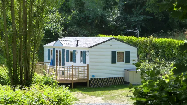 Mobil-home blanc avec terrasse en bois et végétation environnante dans le camping de Coutances