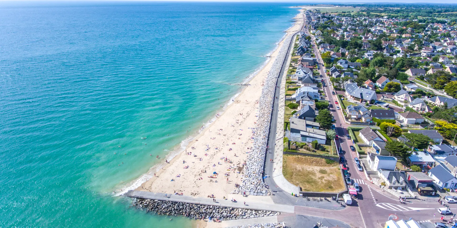 Plage de sable blanc avec des palmiers et des bâtiments en arrière-plan, des personnes sur la promenade