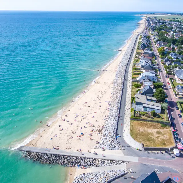 Plage de sable blanc avec des palmiers et des bâtiments en arrière-plan, des personnes sur la promenade