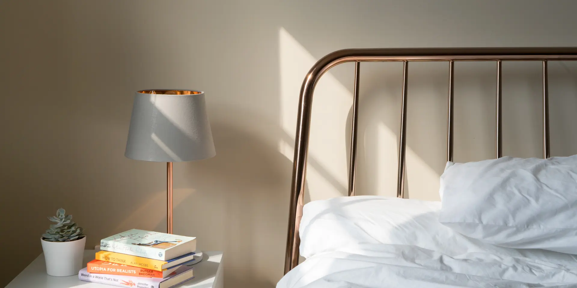 Bett mit einem Metallbettkopf und einer Nachttischlampe neben einem Stapel Bücher