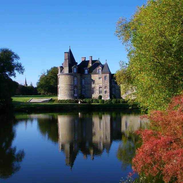 Château médiéval reflété dans l'eau calme d'un lac entouré d'arbres