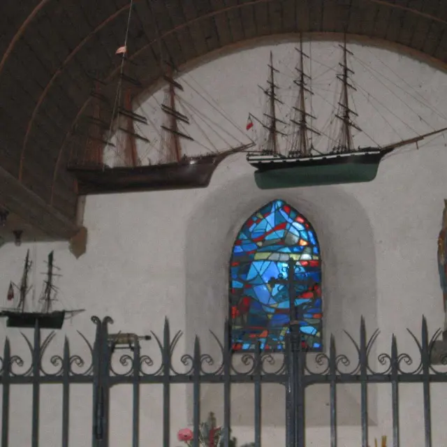 Innenraum einer Kirche mit aufgehängten Schiffmodellen und einer religiösen Statue