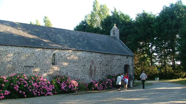 Stone church with a pointed steeple, surrounded by purple flowers and pedestrians