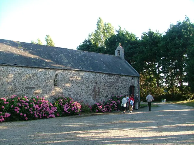 Steinkirche mit spitzem Turm, umgeben von violetten Blumen und Fußgängern
