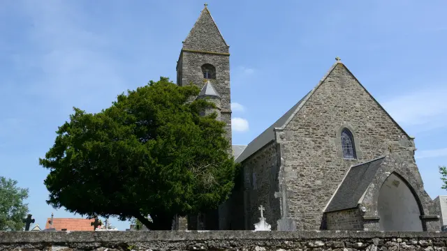 Stone church with a pointed steeple and slate roof, surrounded by green trees