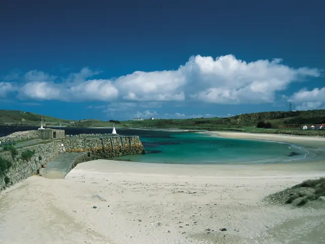 Weißer Sandstrand gesäumt von vertäuten Segelbooten und Gebäuden im Hintergrund unter einem blauen Himmel mit weißen Wolken