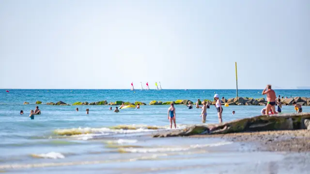 Beach with moored sailboats, yellow umbrellas, and people walking or swimming