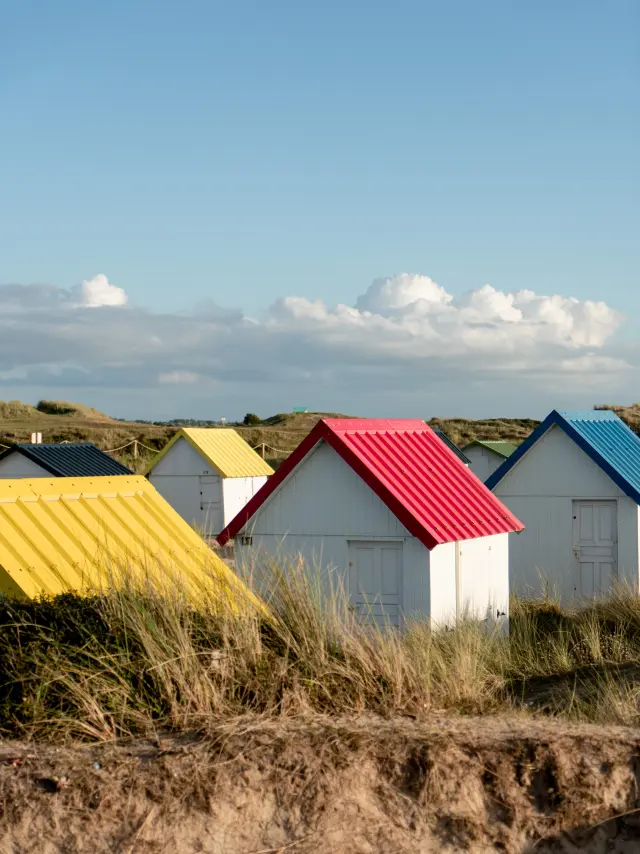 House with blue and bright red walls, white shutters, on a grassy hill facing the sea