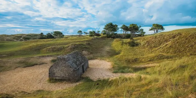 Cabane de douanier en pierre entouré de dunes herbeuses et de quelques arbres