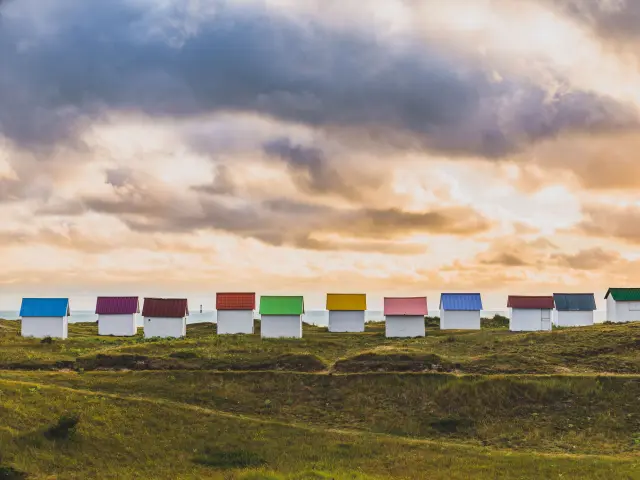 A row of colorful beach huts on a grassy hill at sunset