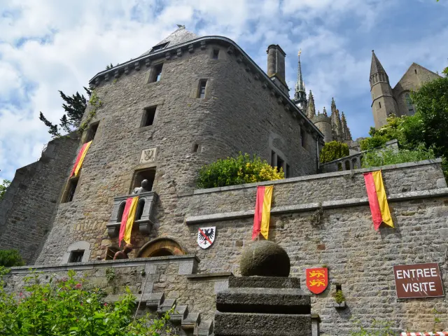 Ancien bâtiment en pierre avec des drapeaux colorés accrochés à une balustrade et une arche en pierre en premier plan