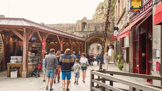 Outdoor market with wooden stalls and people under red umbrellas