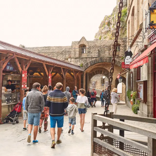 Marché en plein air avec des étals en bois et des passants sous des parasols rouges