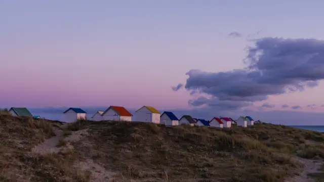 Eine Reihe bunter Strandhütten auf einer Düne beim Sonnenuntergang