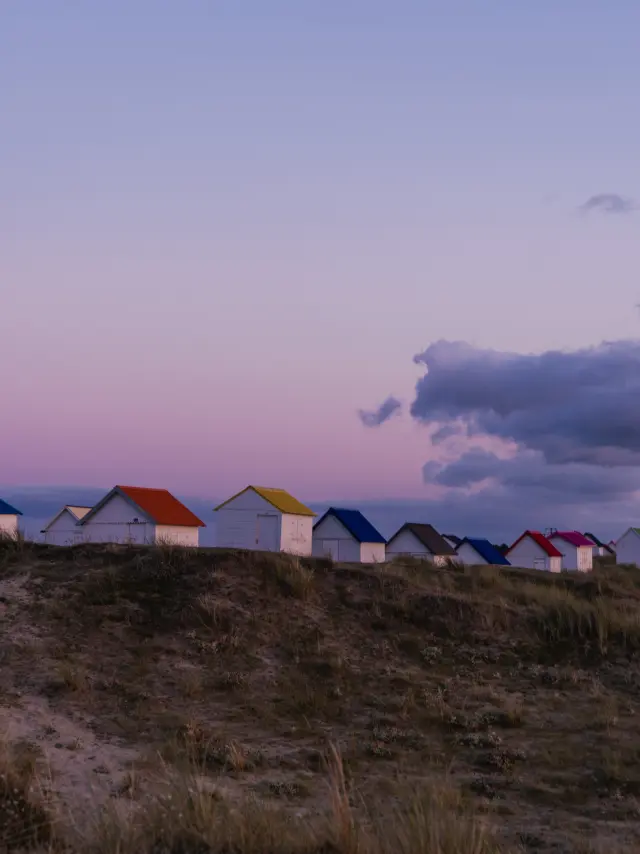 A row of colorful beach huts on a dune at sunset