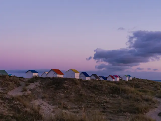 Eine Reihe bunter Strandhütten auf einer Düne beim Sonnenuntergang