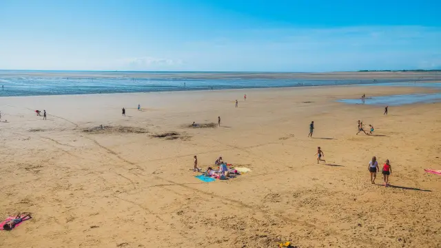Plage de sable avec des personnes se baignant, jouant et se reposant sous un ciel dégagé