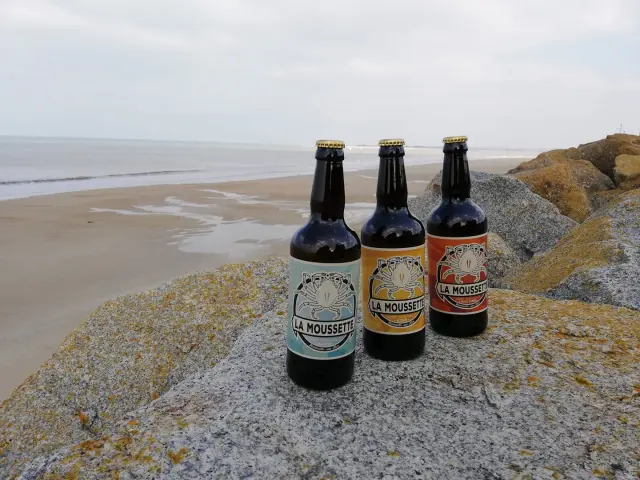 Trois bouteilles de bière La Moussette sur des rochers près de la plage