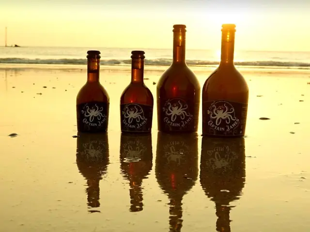 Quatre bouteilles de Captain James sur une plage au coucher du soleil