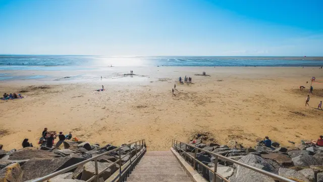 Escaliers menant à une plage de sable avec des gens se relaxant et jouant près de l'eau