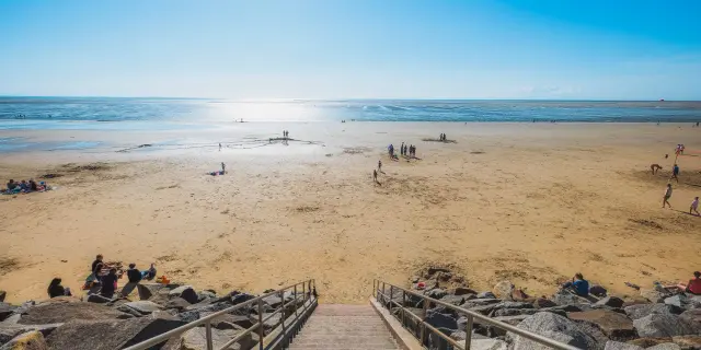 Escaliers menant à une plage de sable avec des gens se relaxant et jouant près de l'eau