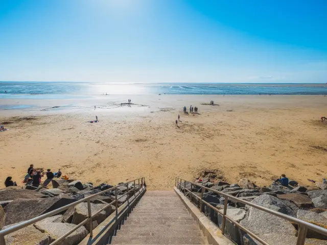 Escaliers menant à une plage de sable avec des gens se relaxant et jouant près de l'eau