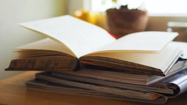 Un livre ouvert sur une pile de livres près d'une fenêtre avec une plante en pot