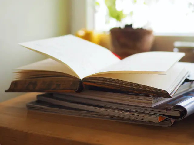 Un livre ouvert sur une pile de livres près d'une fenêtre avec une plante en pot